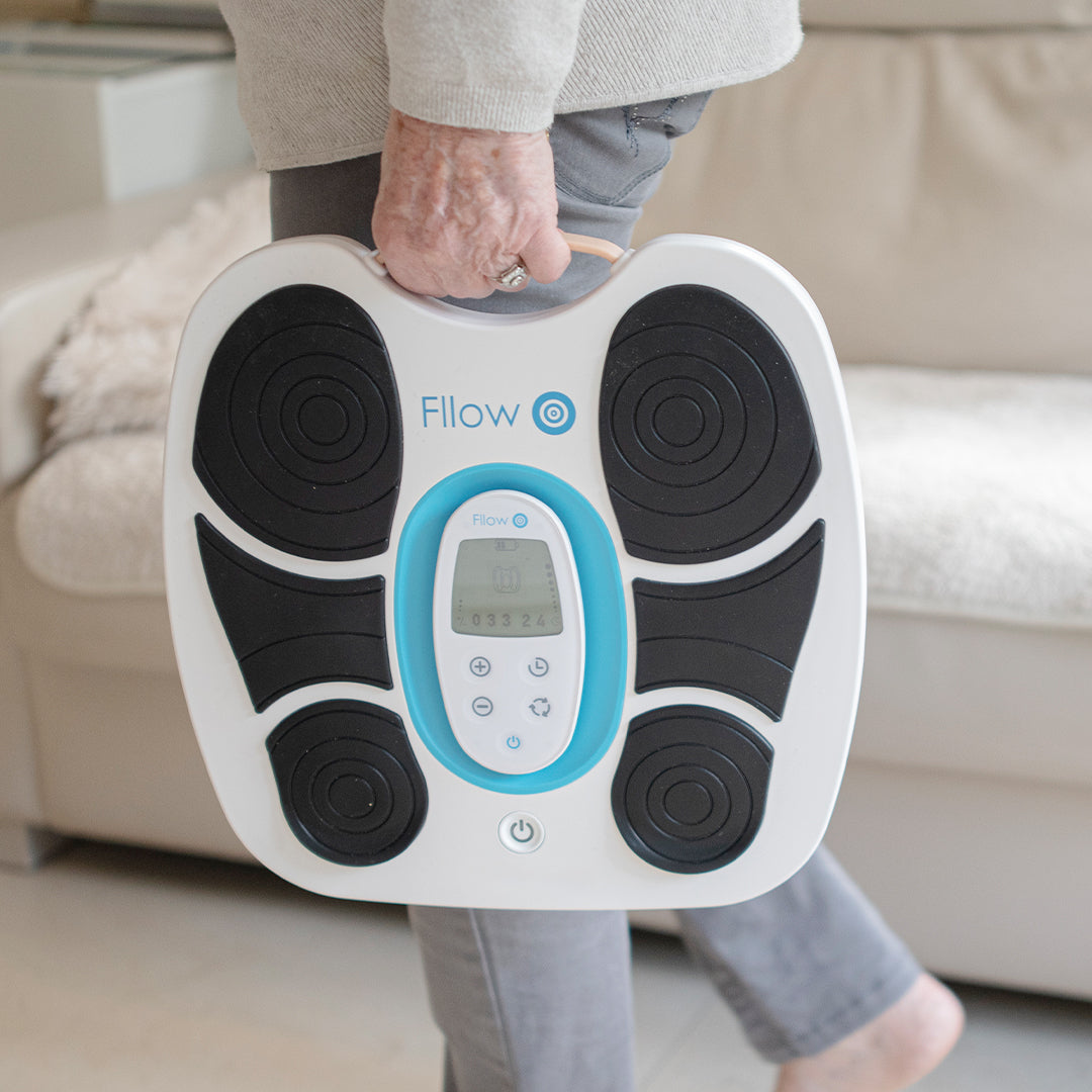Person trägt das Fllow Fußmassagegerät am Griff in der Hand – tragbares, leichtes Design im modernen Look.