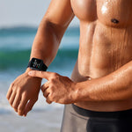 Ein sportlicher Mann steht am Strand und bedient den Kendox LifeTracker zur Trainingskontrolle.