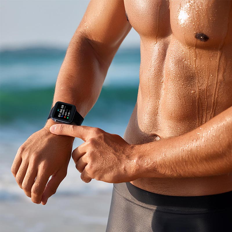 Ein sportlicher Mann steht am Strand und bedient den Kendox LifeTracker zur Trainingskontrolle.