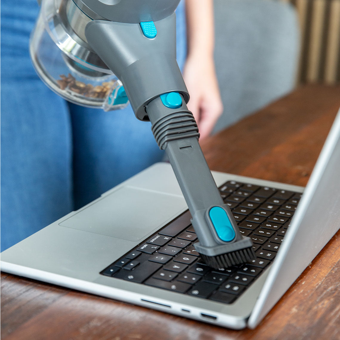 Ein Akkusauger reinigt mit Bürstenaufsatz vorsichtig eine Laptop-Tastatur.