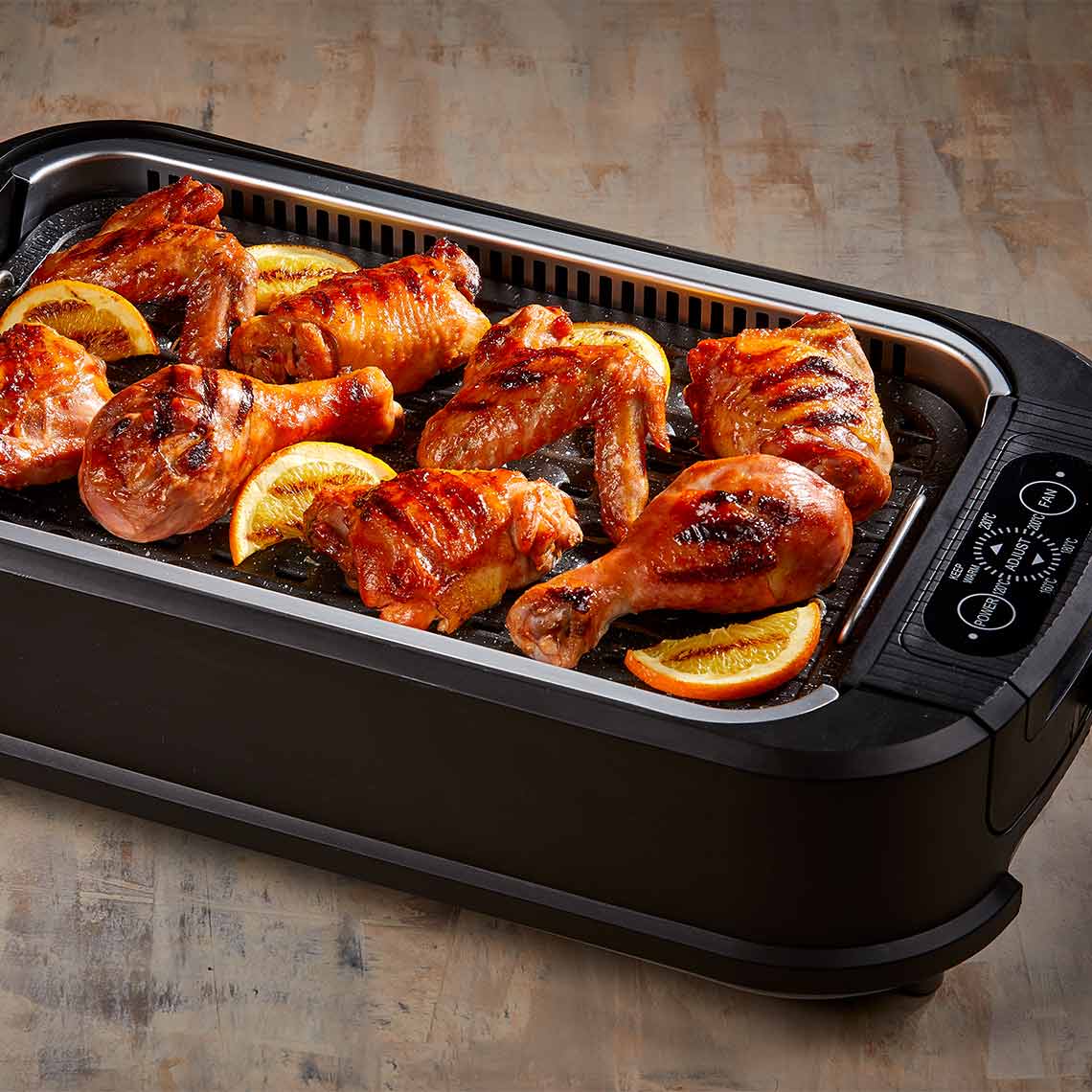 PowerXL Smokeless Grill – gegrillte Hähnchenteile mit Orangenscheiben auf Grillplatte, appetitlich angerichtet.