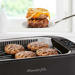 PowerXL Smokeless Grill – saftige Burger auf Grillplatte, einer mit Käse und Zwiebel wird serviert.