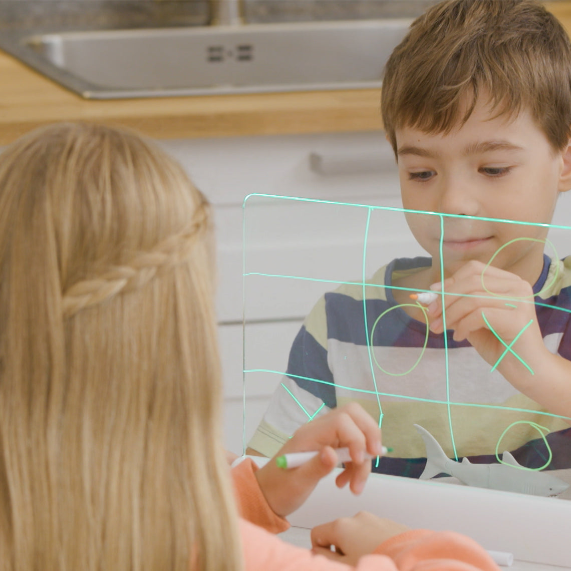 Zwei Kinder spielen Tic-Tac-Toe auf einer beleuchteten Mini-Leuchttafel.