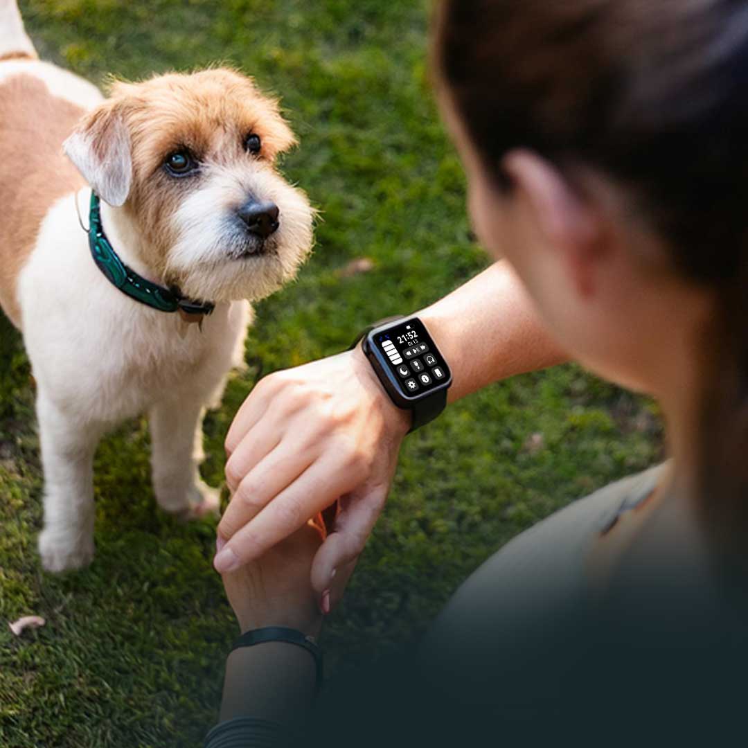 Frau im Freien bedient den Kendox LifeTracker am Handgelenk, ein Hund sitzt vor ihr auf dem Rasen.