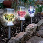Drei Solar LED Leuchten mit farbigem Licht stehen in einem Gartenbeet zwischen Steinen und Pflanzen.