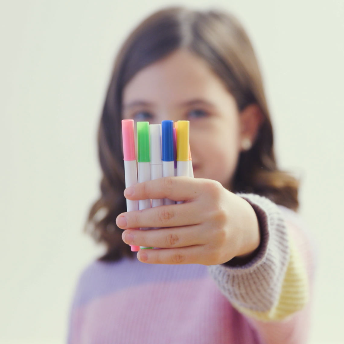 Mädchen hält vier bunte Filzstifte in der Hand vor sich.