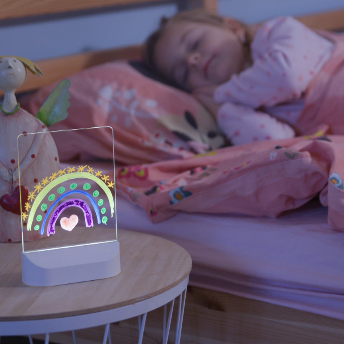 Leuchtendes Mini-Leuchtboard mit Regenbogenmotiv auf dem Nachttisch neben schlafendem Kind.