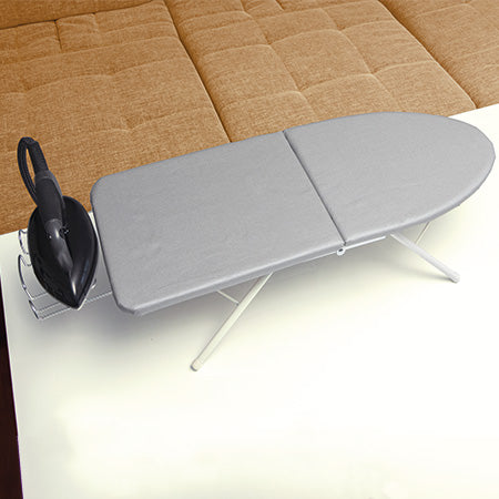 Faltbares Tischbügelbrett mit Metallgestell und Bügeleisenablage, auf einem Tisch vor einem Sofa aufgestellt.