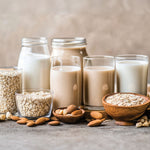 Verschiedene pflanzliche Milchsorten und Zutaten wie Hafer und Mandeln in Gläsern arrangiert.