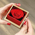 Hände halten eine kleine Box mit roter konservierter Rose und einem drehbaren seitlichen Element.
