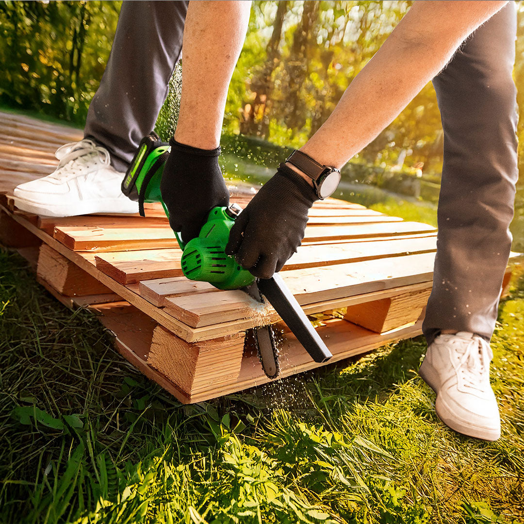 Person zersägt im Garten eine Holzpalette mit einer Mini-Kettensäge.