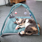 Katze liegt entspannt auf einer Spiel- und Kuschelmatte mit vier hängenden Spielzeugen unter einem Bogen.