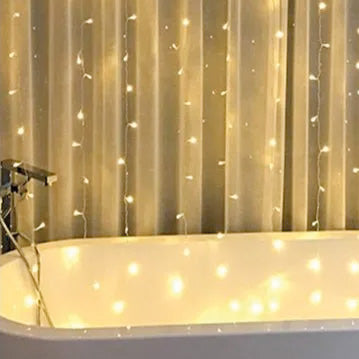 LED-Lichterketten hängen vor Duschvorhang, warmes Licht spiegelt sich in der Badewanne.