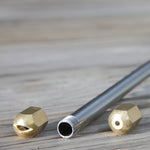 Ein Metallsprührohr mit Gewinde liegt neben zwei auswechselbaren Messingdüsen.