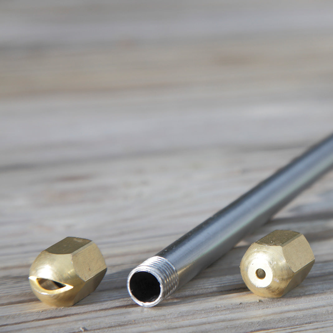 Ein Metallsprührohr mit Gewinde liegt neben zwei auswechselbaren Messingdüsen.