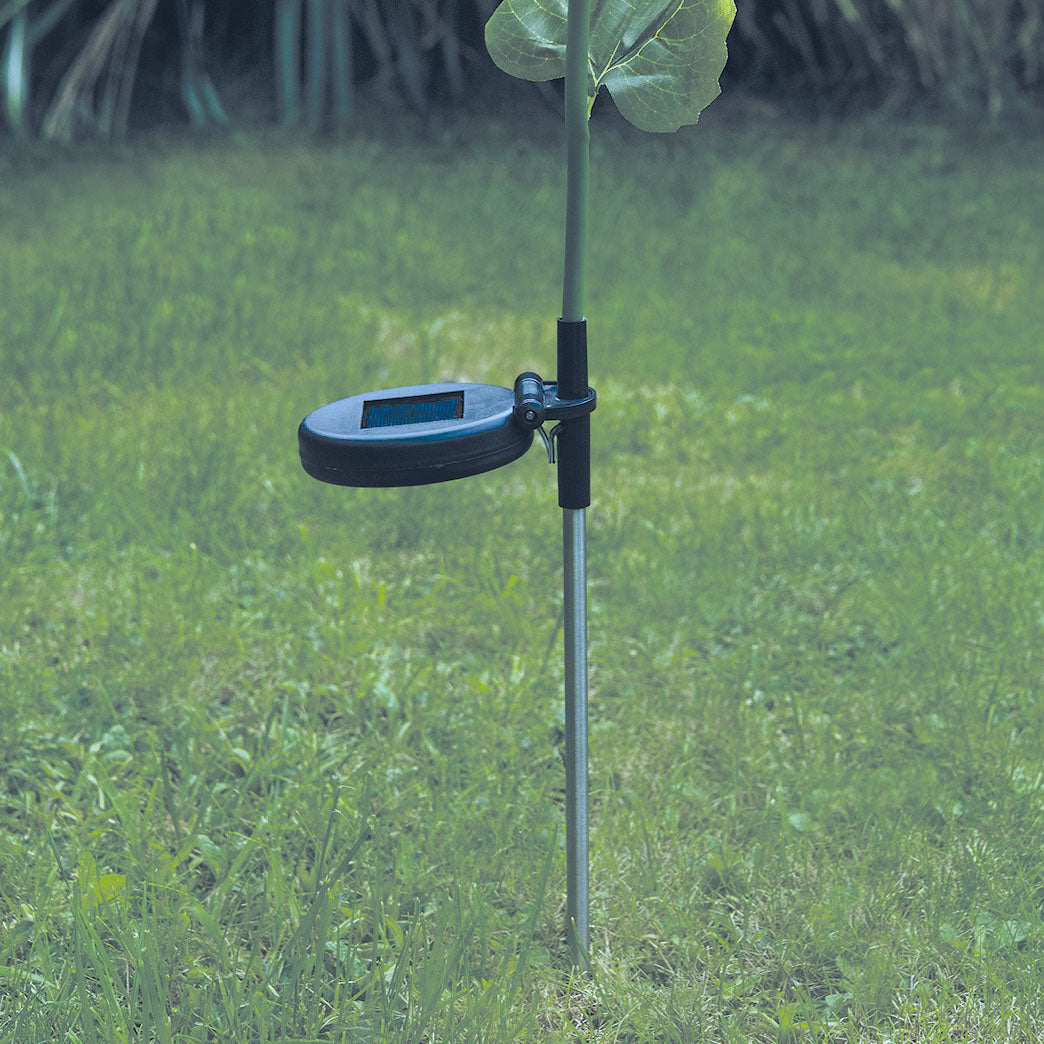 Ein kleines Solarpanel ist mittig an einem Blumenstiel im Garten montiert.