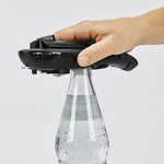 Der schwarze 5in1-Multiöffner wird zum Öffnen eines Kronkorkens auf einer Glasflasche angesetzt – ergonomische Handhabung.