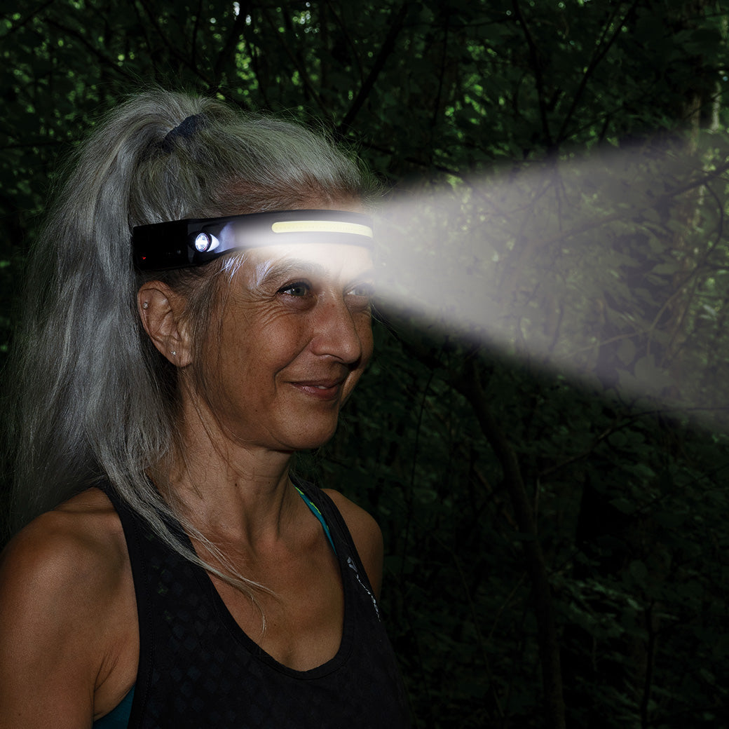 Frau draußen im Dunkeln - Lichtstrahl der Stirnlampe erhellt die Umgebung.
