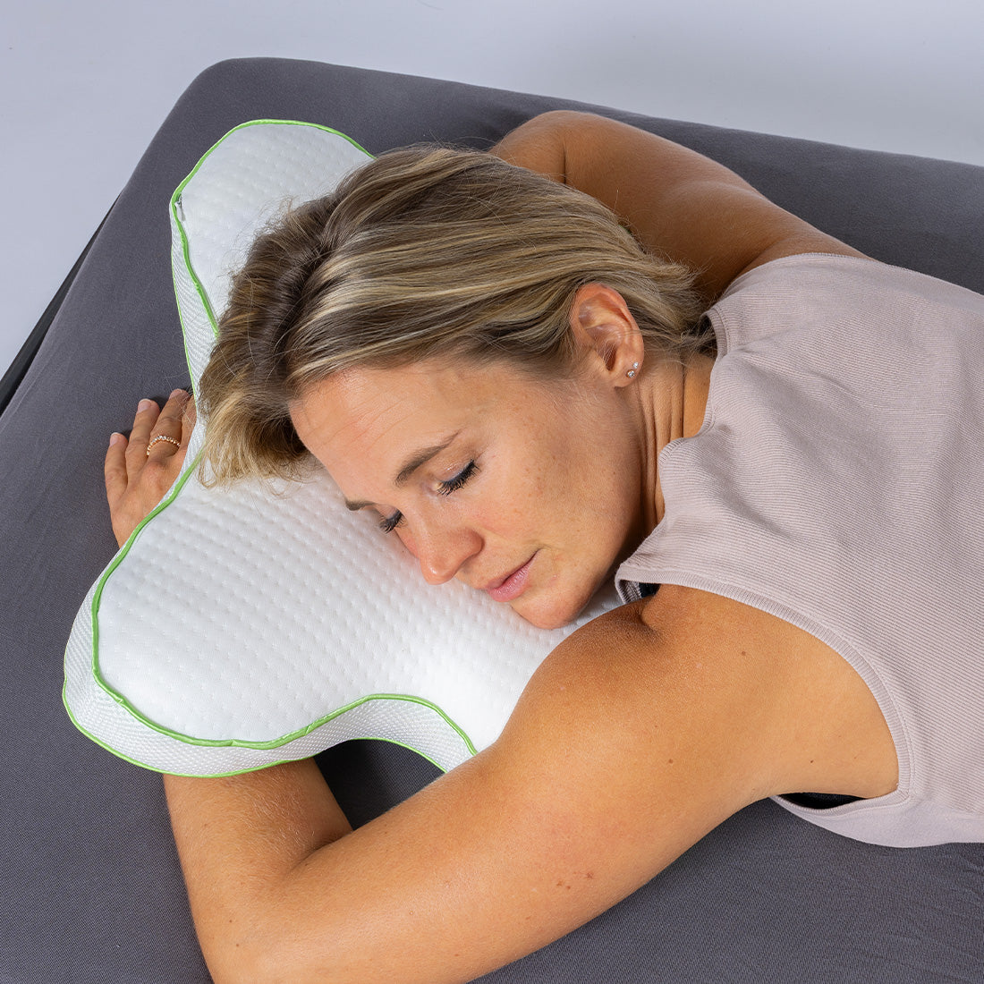 Frau liegt entspannt auf einem weißen, ergonomisch geformten Schmetterlingskissen mit grünem Rand.