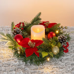 Weihnachtskranz mit LED-Kerze in der Mitte, roten Blüten, Tannenzweigen, Kugeln, Zapfen und Beeren dekoriert.