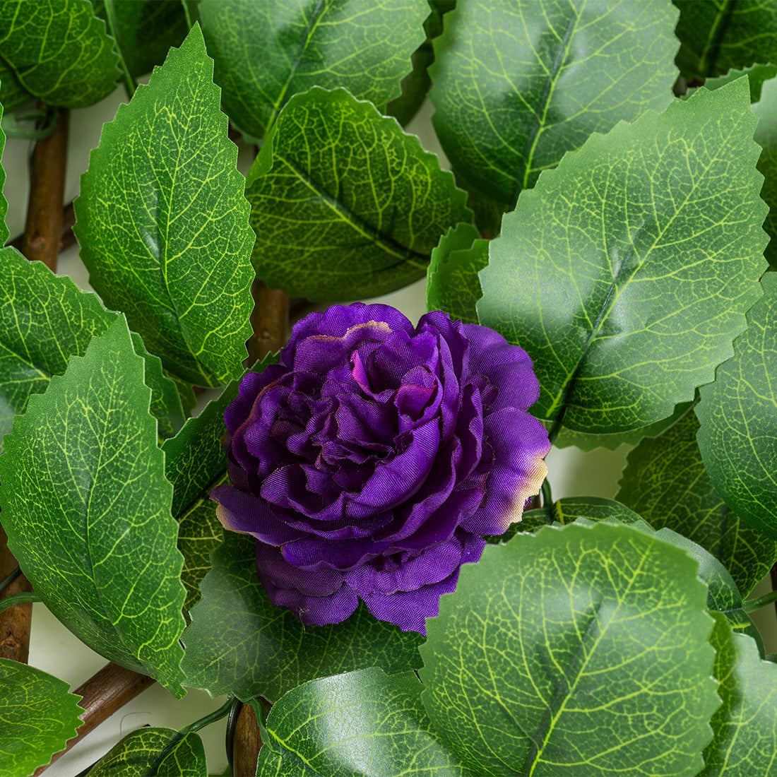 Detailaufnahme einer künstlichen violetten Rosenblüte, umgeben von täuschend echtem Kunststoff-Laub