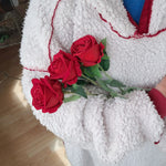 Person hält drei künstliche rote Rosen mit grünen Blättern, getragen wird eine flauschige Jacke.