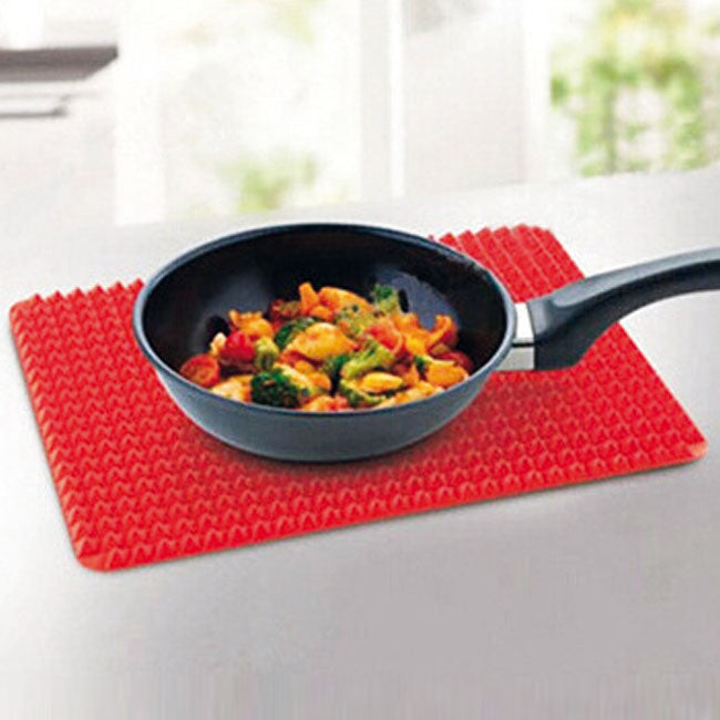 Bratpfanne mit Gemüse steht auf roter, genoppter Silikonmatte auf einer Arbeitsfläche.