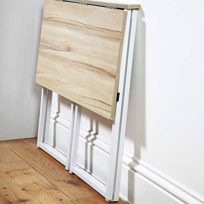 Zusammengeklappter Falt-Tisch mit Holzplatte und weißem Metallgestell, stehend an einer Wand.